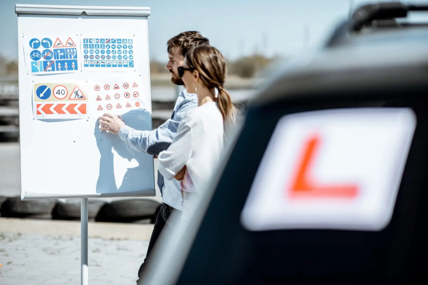 Driving instructor going through road signs with a learner beside an L-plate car